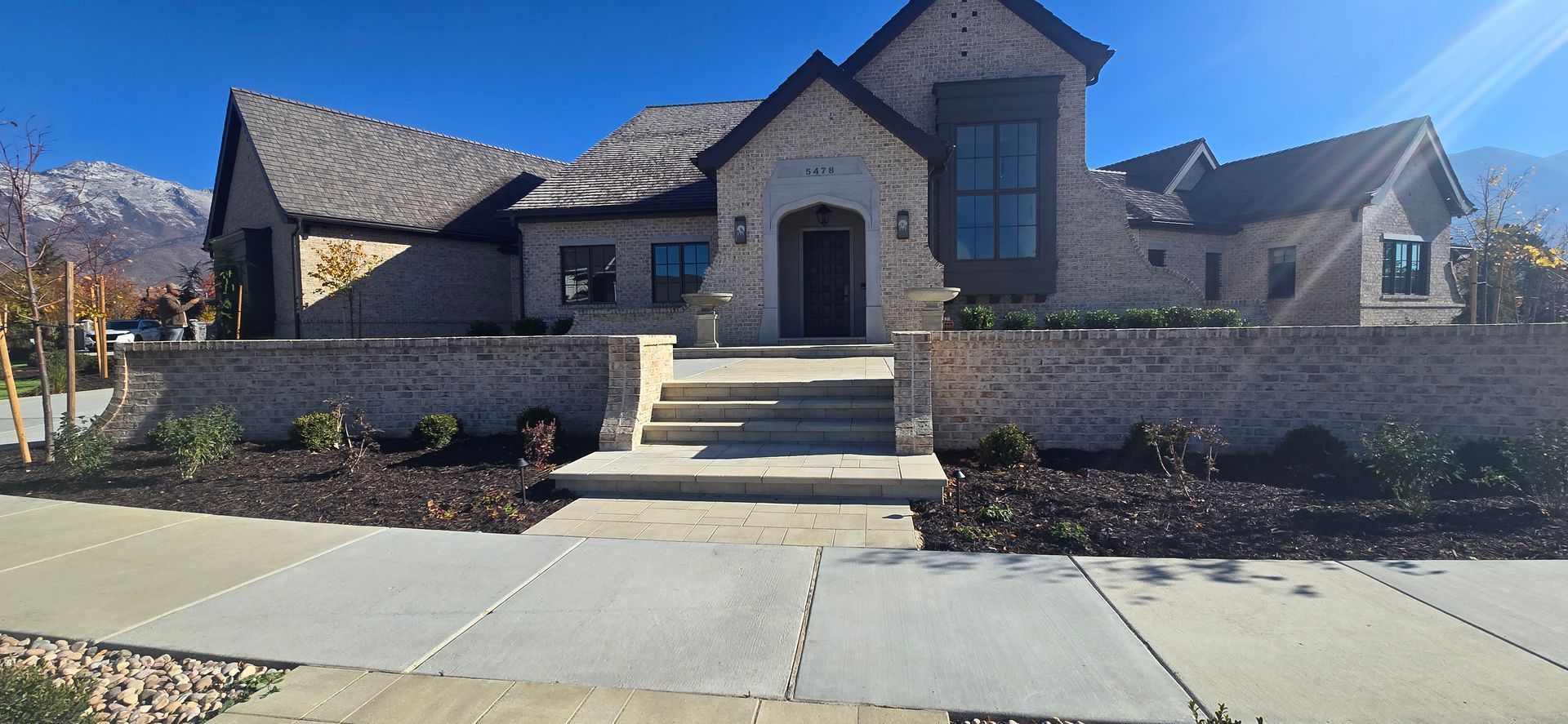 Stone house with steps, front walkway, and landscaped yard under a clear blue sky