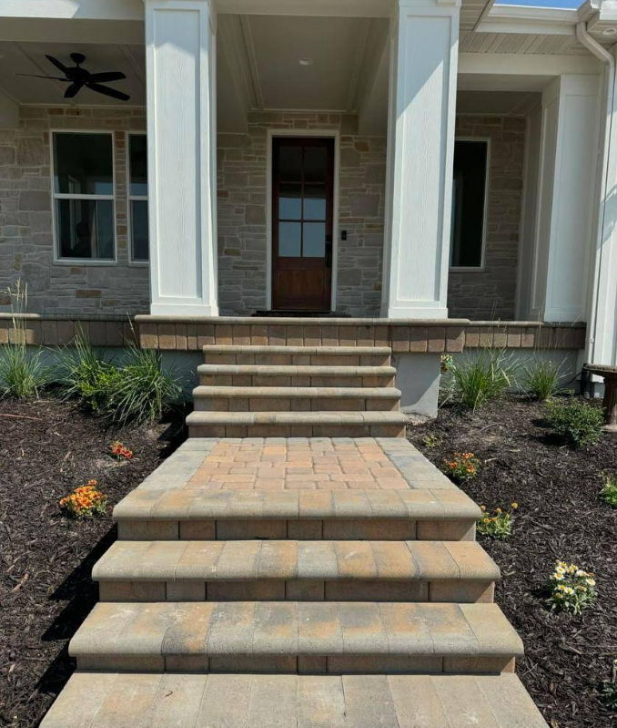 Front porch with brick steps, tan paver landing, and white columns on a house exterior.