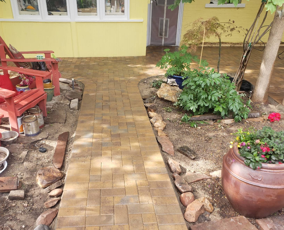 Brick walkway through a small garden courtyard beside a yellow house and red bench