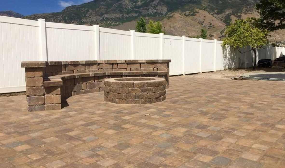 Stone outdoor seating area on a paver patio beside a white fence, with mountains in the background