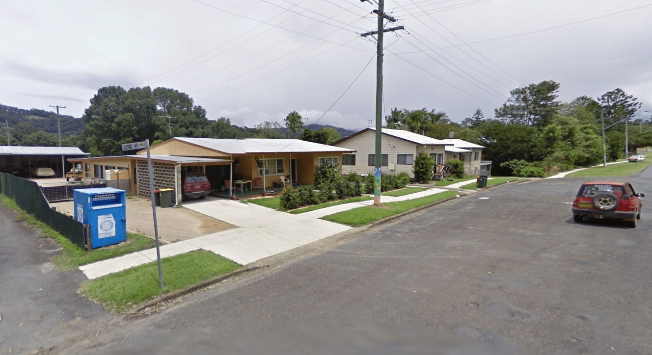 A Red Car Is Driving Down a Street Next to A Row of Houses — Murwillumbah District Plumbing Service in Burringbar, NSW