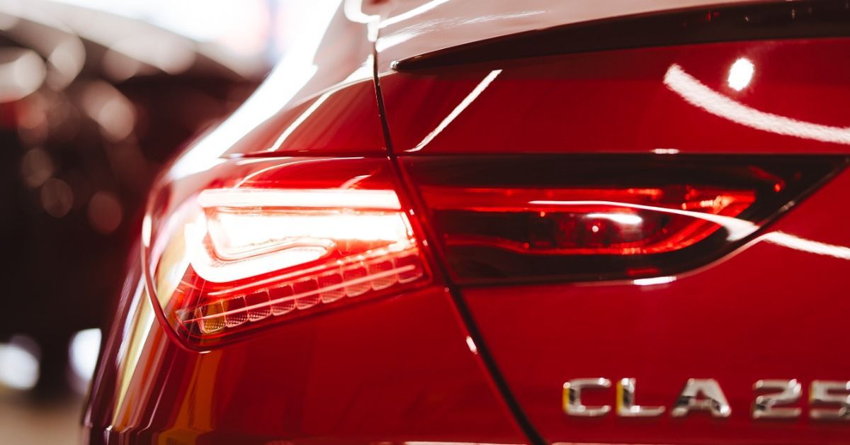 A close-up of a red vehicle taillight and rear panel with bright reflections across the paint indoor