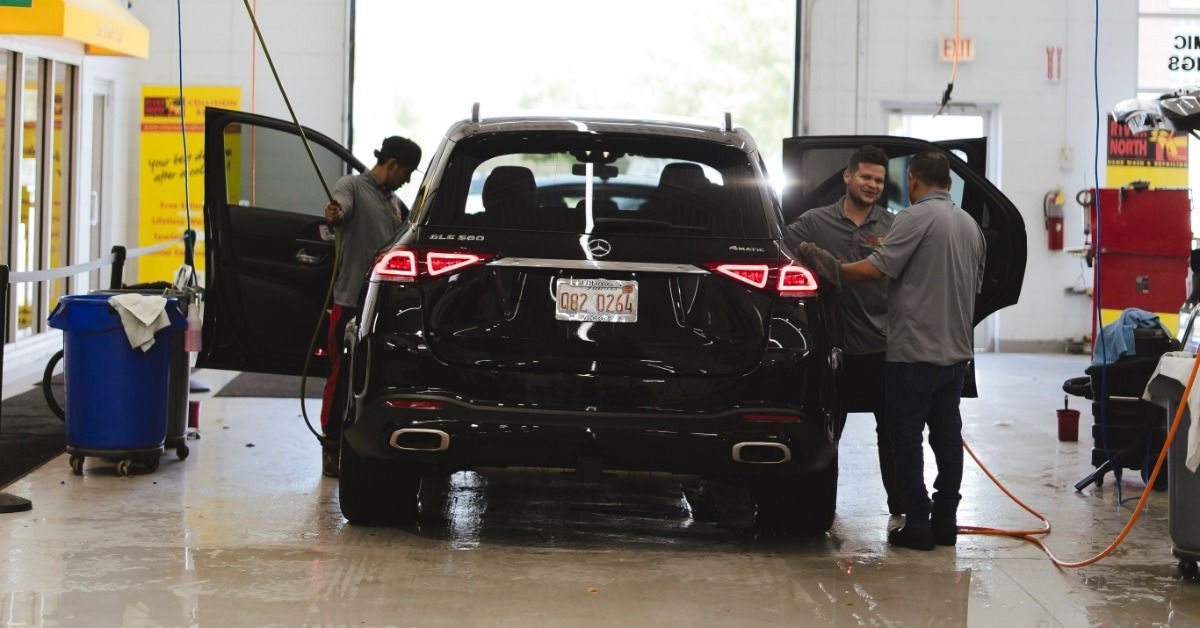 A black SUV with open doors inside an automotive service shop. Three people are working around the vehicle.