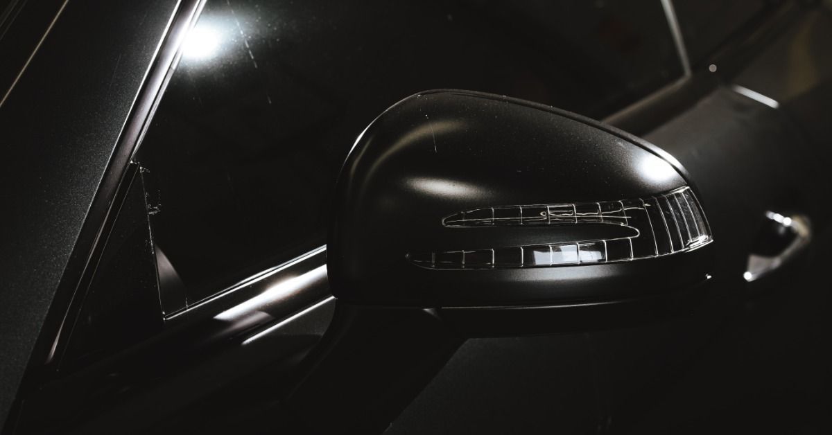 A black car's side mirror with an integrated turn signal beside a dark tinted window and glossy door panel.