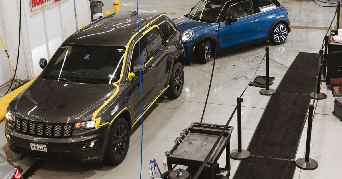 Two cars lined up inside a car wash bay with taped trim on one side. The floors are wet under the vehicles.