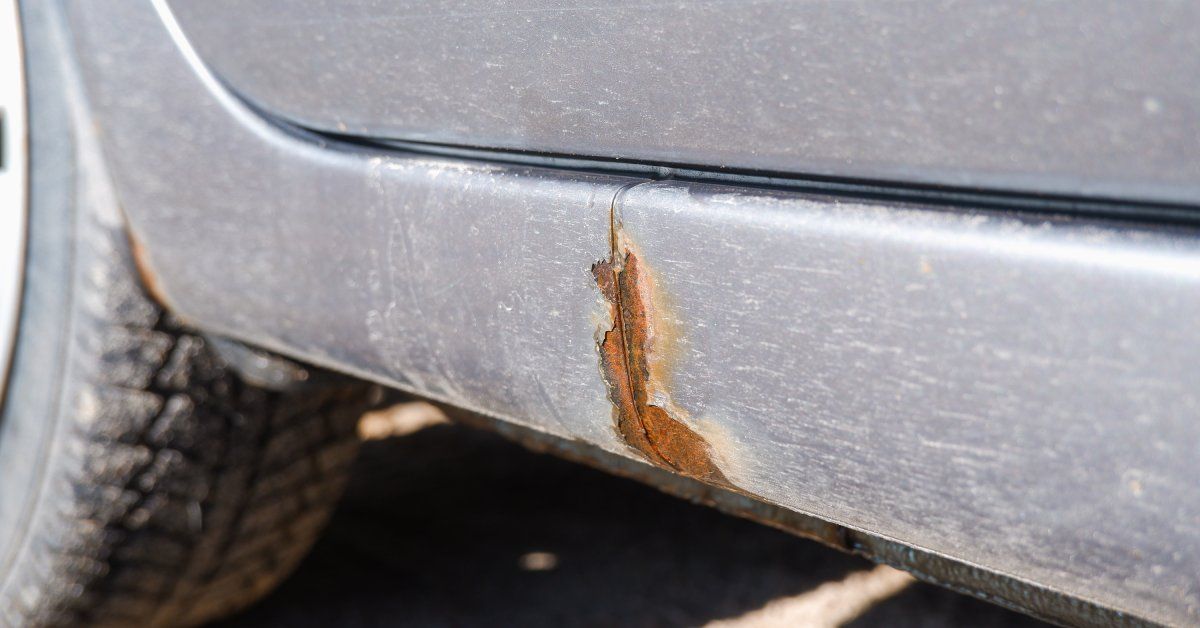 A car that has paint chipping and rust forming underneath the rear door.