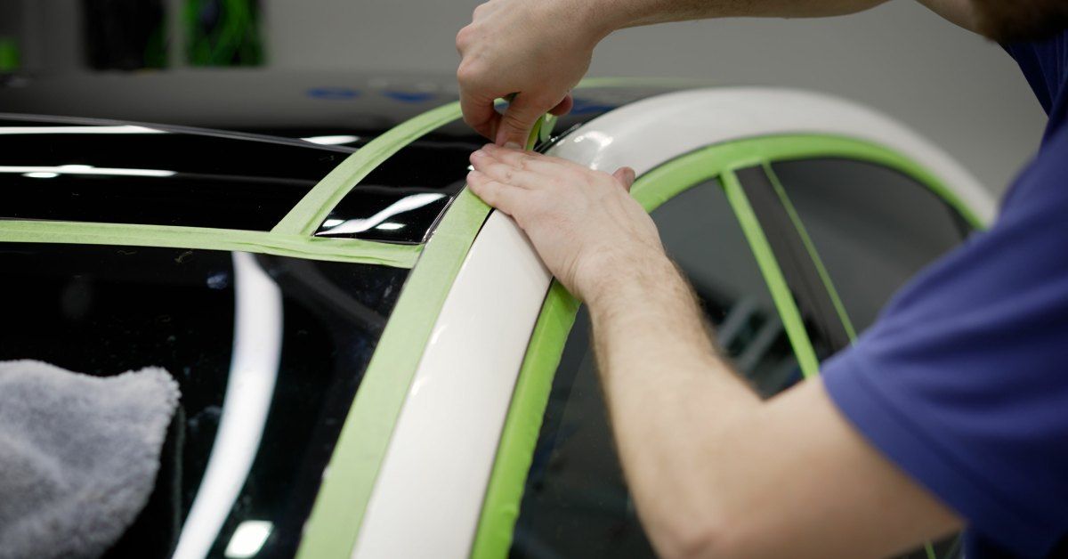  A car detailer wrapping a car in green vinyl tape. He is preparing and protecting the surface for a custom body paint job.