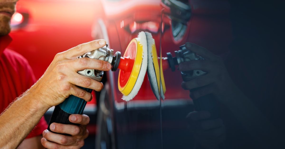 A car detail shop restoration specialist polishing a car's exterior with a tool. He is holding the tool carefully.