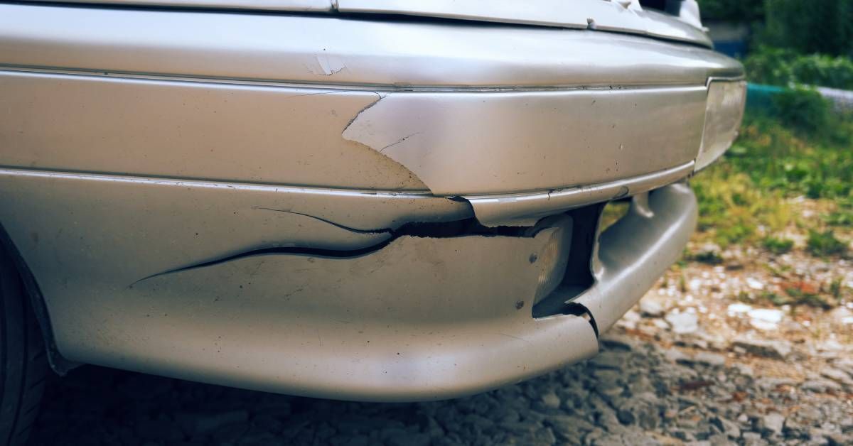 A cracked front bumper on a silver car. The crack expands from the front to the side of the bumper near the tire.