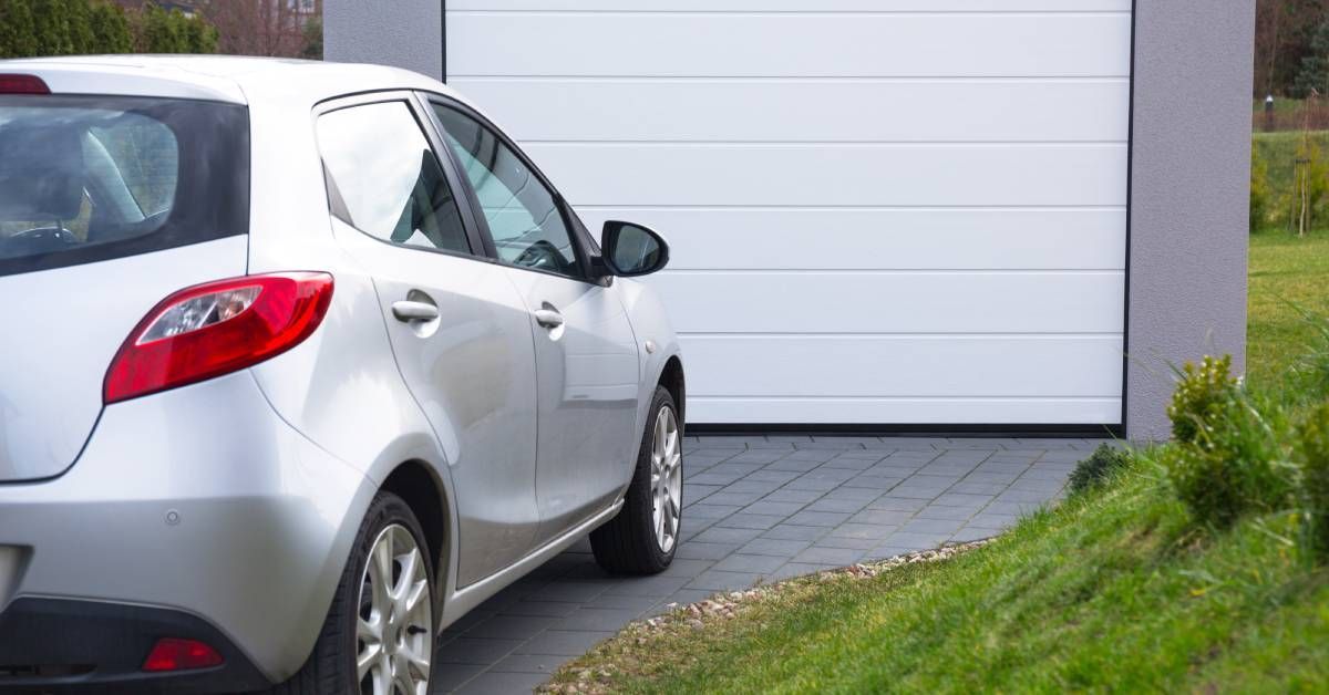 A white car parked on a driveway in front of a residential garage. Around the driveway, there are patches of green grass.