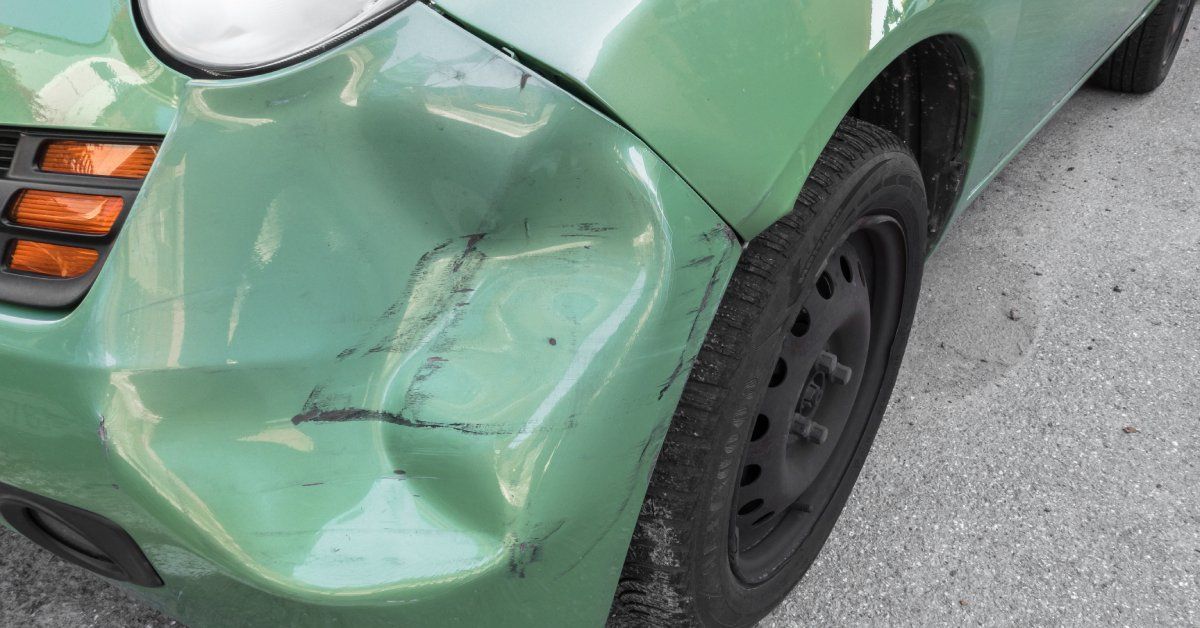 A bright green car with a large dent on the driver side. The dent is underneath the headlight with black scuff marks.