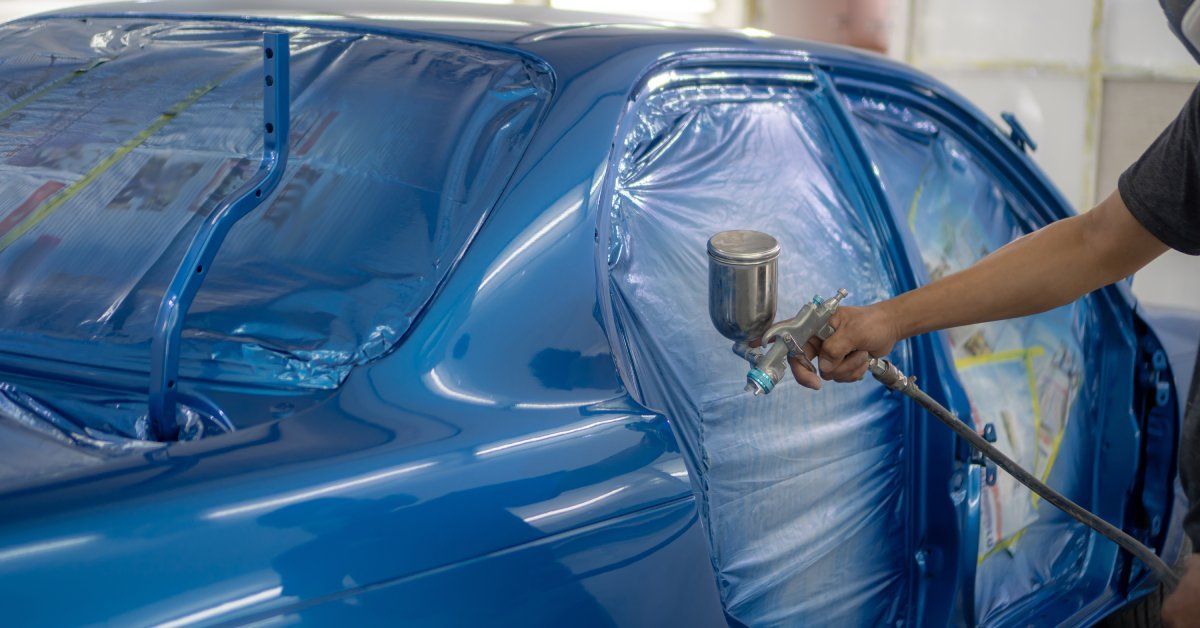 A worker painting the exterior of a car blue. Inside the car, the area is sealed to prevent paint from getting in.