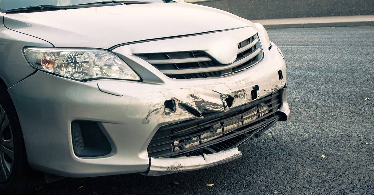 The front of a vehicle with damage to the bumper. There are scrapes, and part of the bumper is missing.