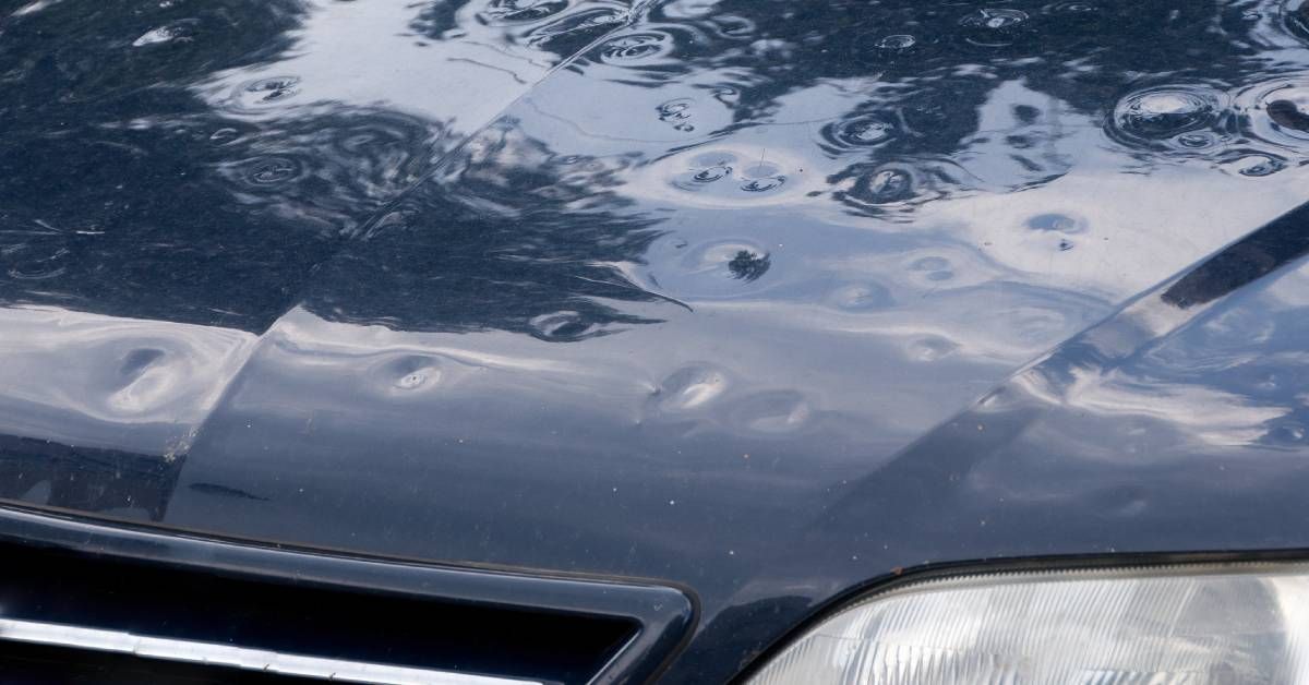 Small dents on a black car caused by a hailstorm vary in depth and size. They are scattered across the hood.