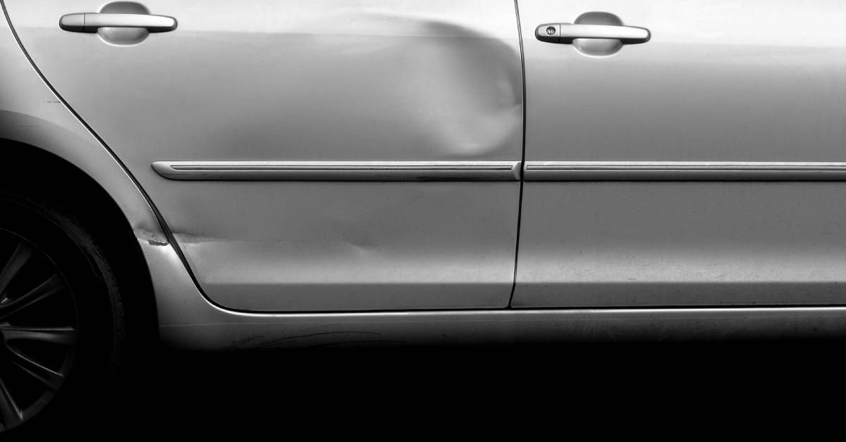 A standard gray sedan with a noticeable dent in the rear passenger side door. It may require professional repair.