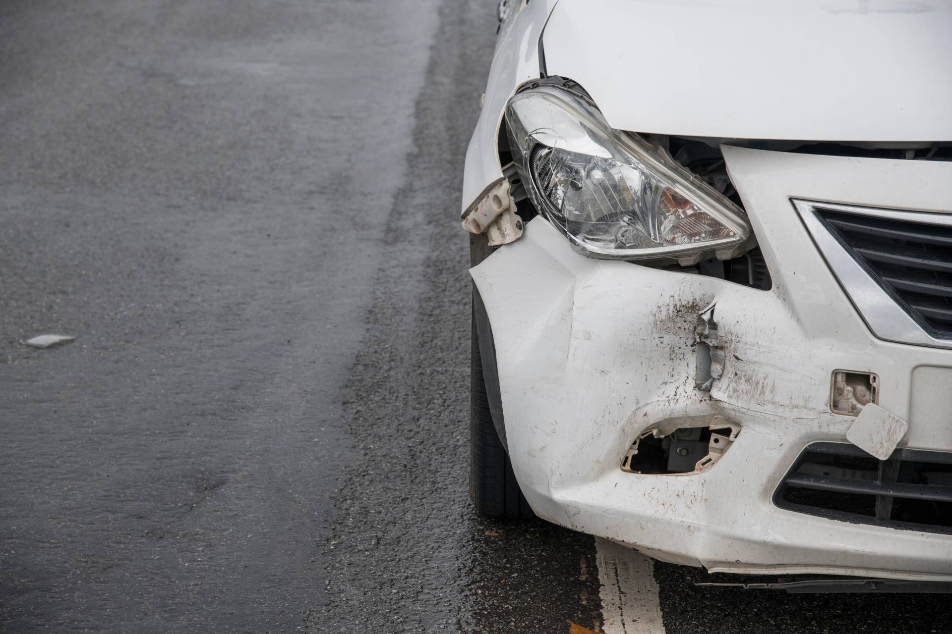 A small white sedan that was just recently in an accident. The front bumper is horribly dented and cracked.