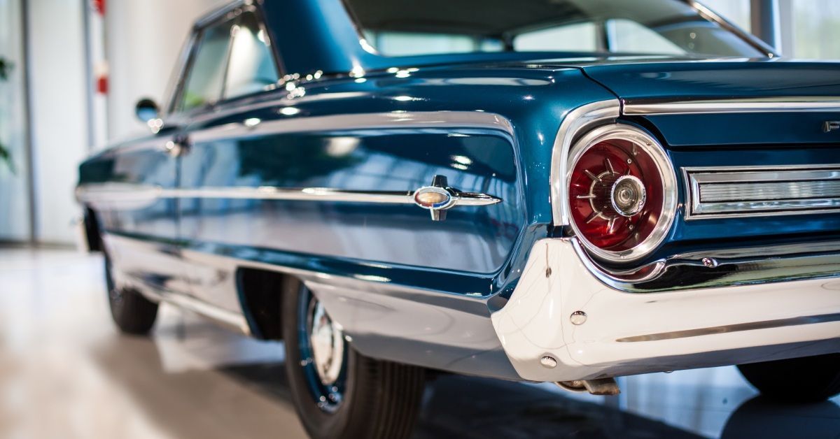 A bright blue classic car with a gorgeous chrome trim. It faces away, with the left rear light visible.