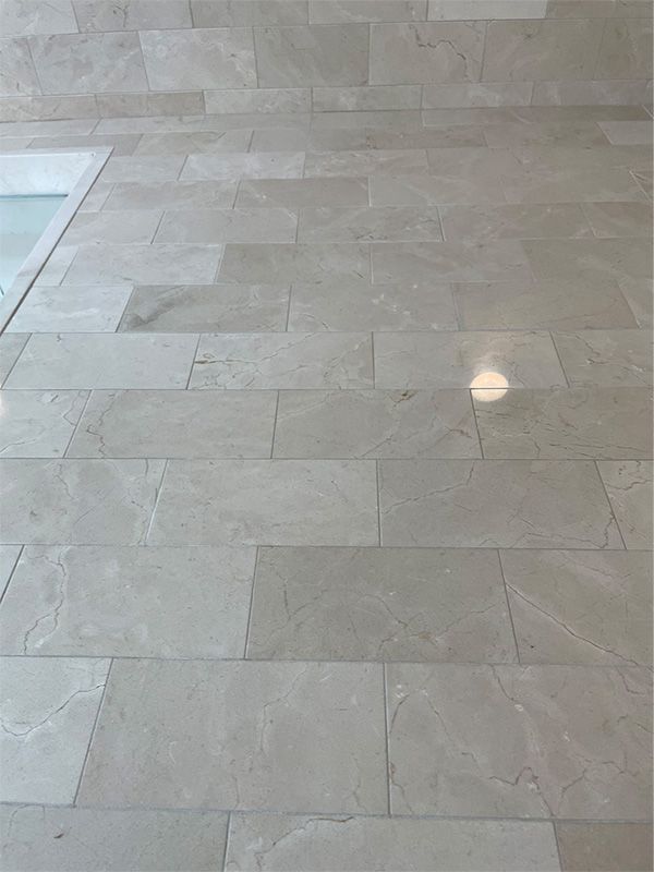A close up of a tiled floor with a bathtub in the background.