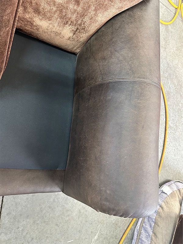 A brown leather couch is sitting on a concrete floor next to a yellow cord.