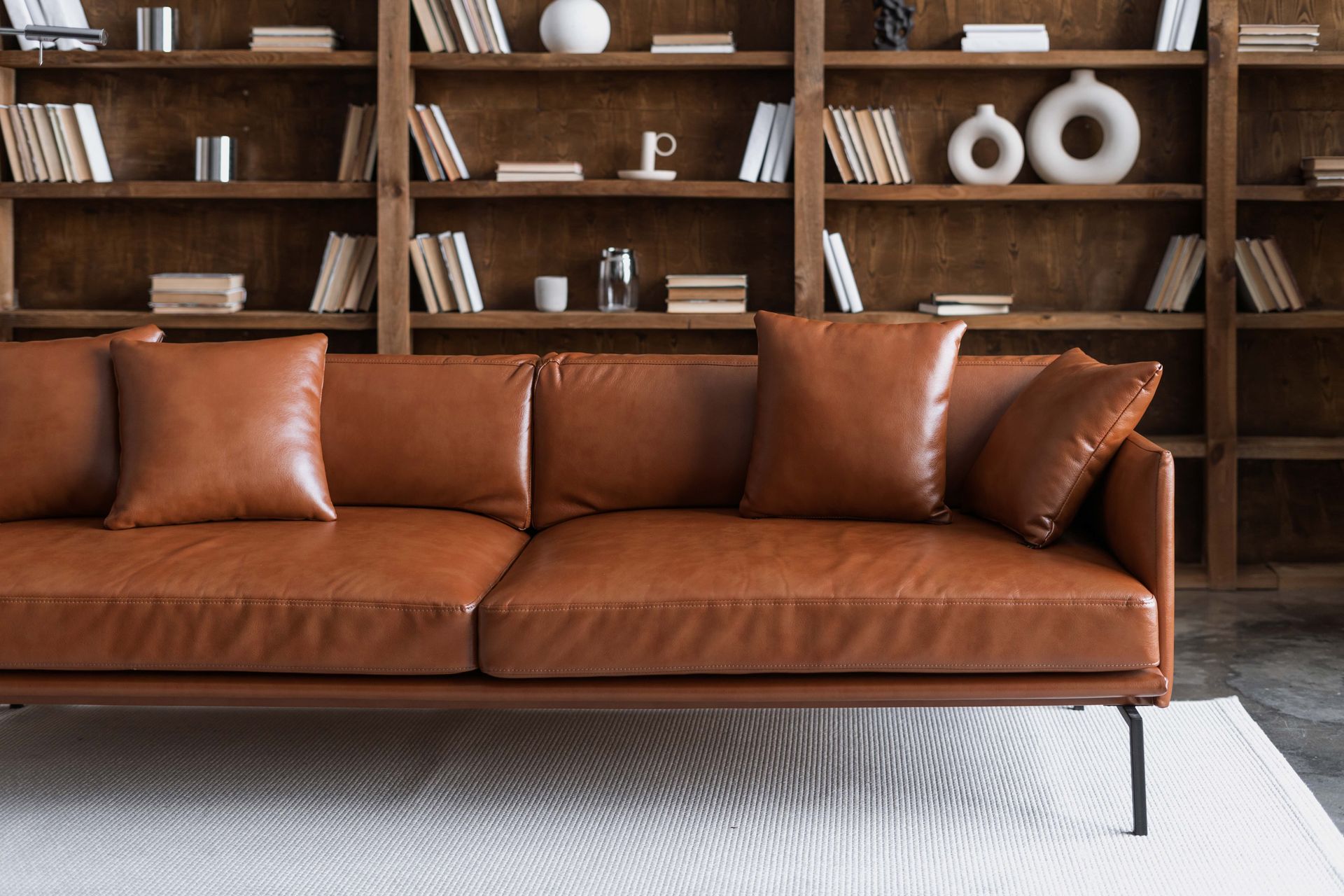 A brown leather couch is sitting in front of a bookshelf in a living room.