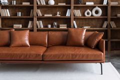 A brown leather couch is sitting in front of a bookshelf in a living room.