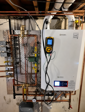 Utility room with wall-mounted boiler, pipes, and a yellow handheld meter attached to the unit.