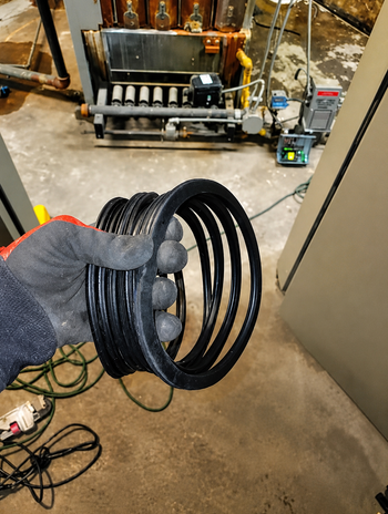 Gloved hand holding coiled black cable in a workshop with machinery in the background