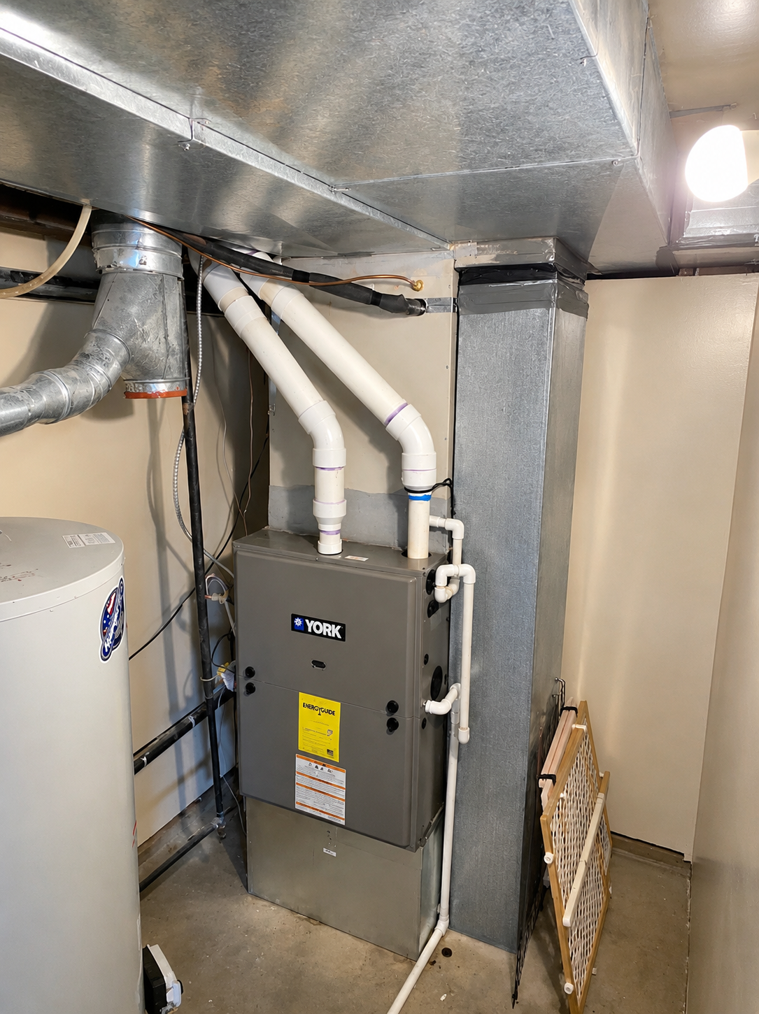 HVAC furnace and ductwork in a basement utility closet with metal vents and white PVC pipes