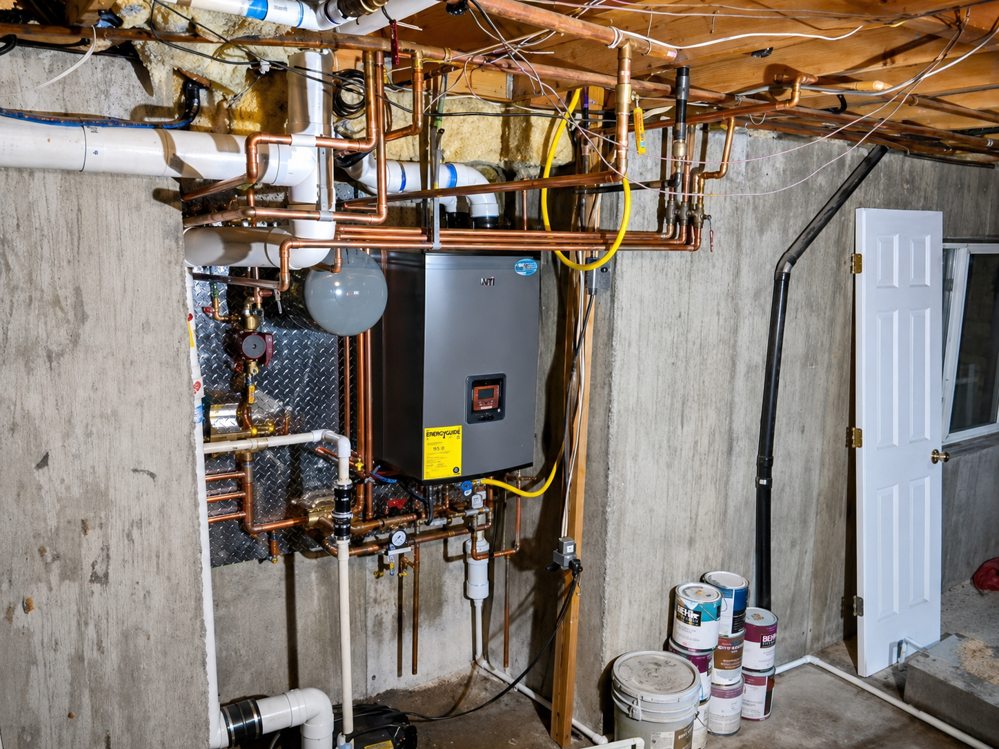 Basement utility area with boiler, copper pipes, exposed wiring, and paint buckets near a door.