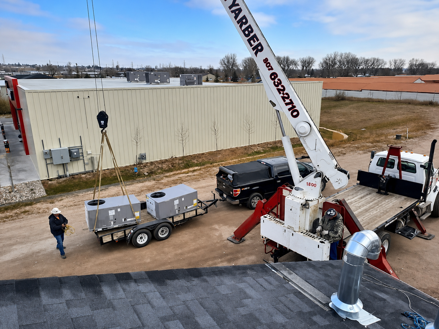 Crane lifting a large HVAC unit beside a beige industrial building, with workers and trucks nearby.