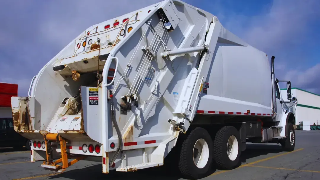 A white garbage truck is parked in a parking lot