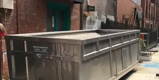 8-yard dumspster A large stainless steel dumpster is parked in front of a brick building.
