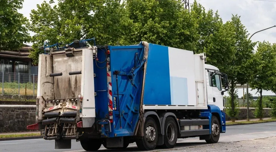 A blue and white garbage truck is driving down a street.