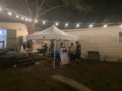 A group of people are standing under a tent in a backyard at night.