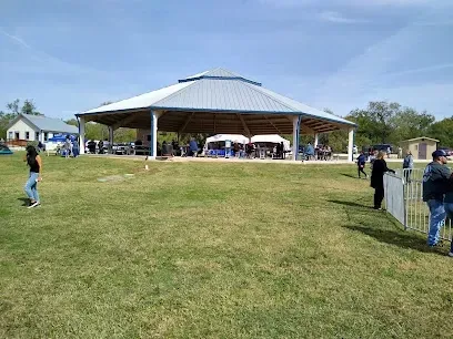 A group of people are standing in a grassy field in front of a pavilion.