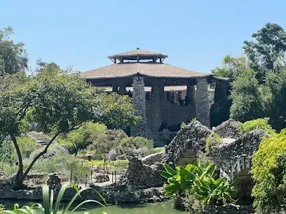 A large stone building is surrounded by trees and a pond.