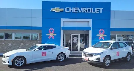 Two white cars are parked in front of a chevrolet dealership.