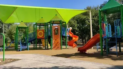 A playground with a slide and a green umbrella in a park.