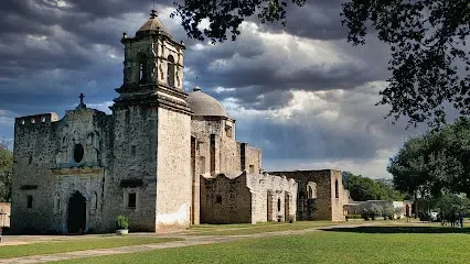 A large stone building with a clock tower is surrounded by grass and trees.