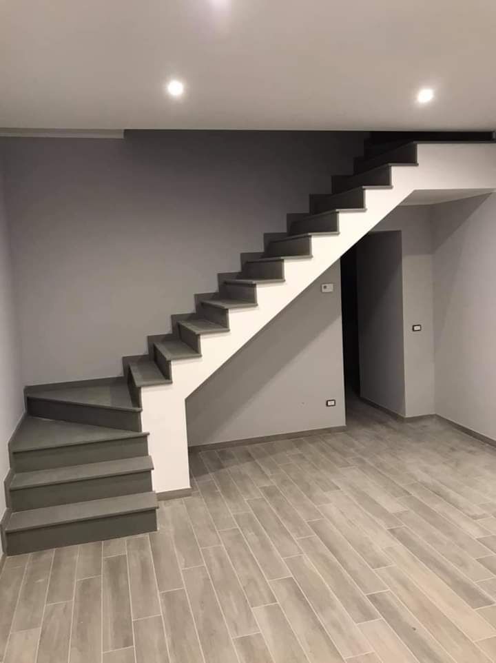Stanza moderna vuota con scala grigia lungo la parete e pavimento in legno chiaro.