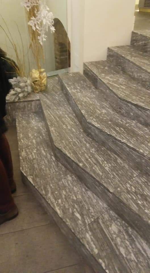 Scala interna in marmo grigio accanto a un vaso decorativo e una composizione di piante dorate.