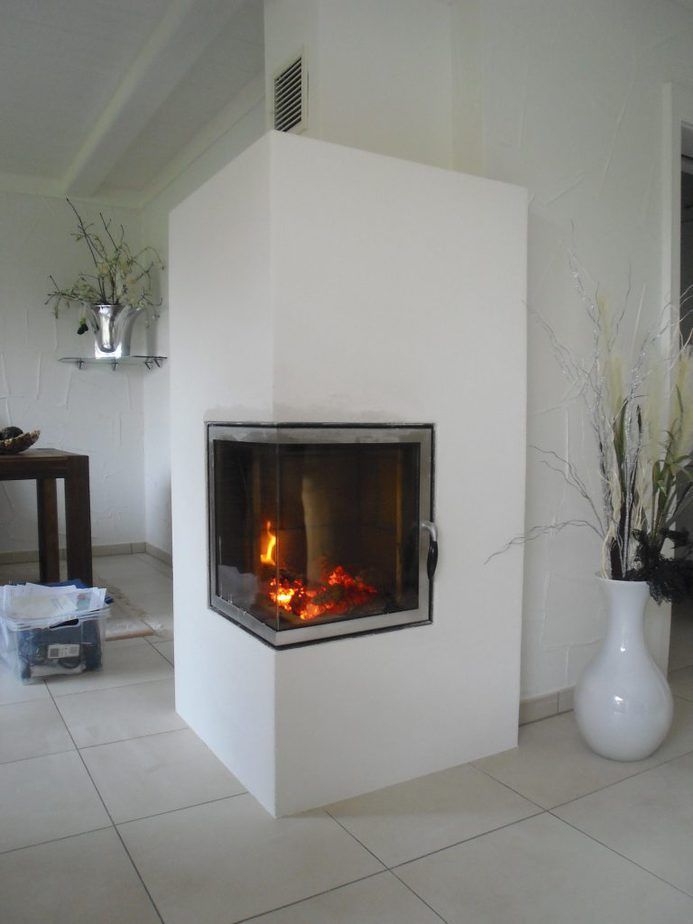 Moderner weißer Eckkamin mit gläsernem Feuerraum in einem hell gefliesten Wohnzimmer.