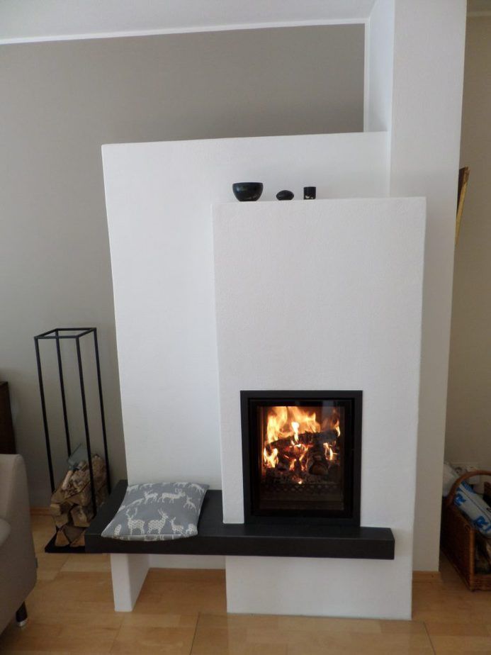 Moderner weißer Kamin mit brennendem Feuer, schwarzer Kaminplatte und kleinen Dekorationselementen in einem Wohnzimmer.