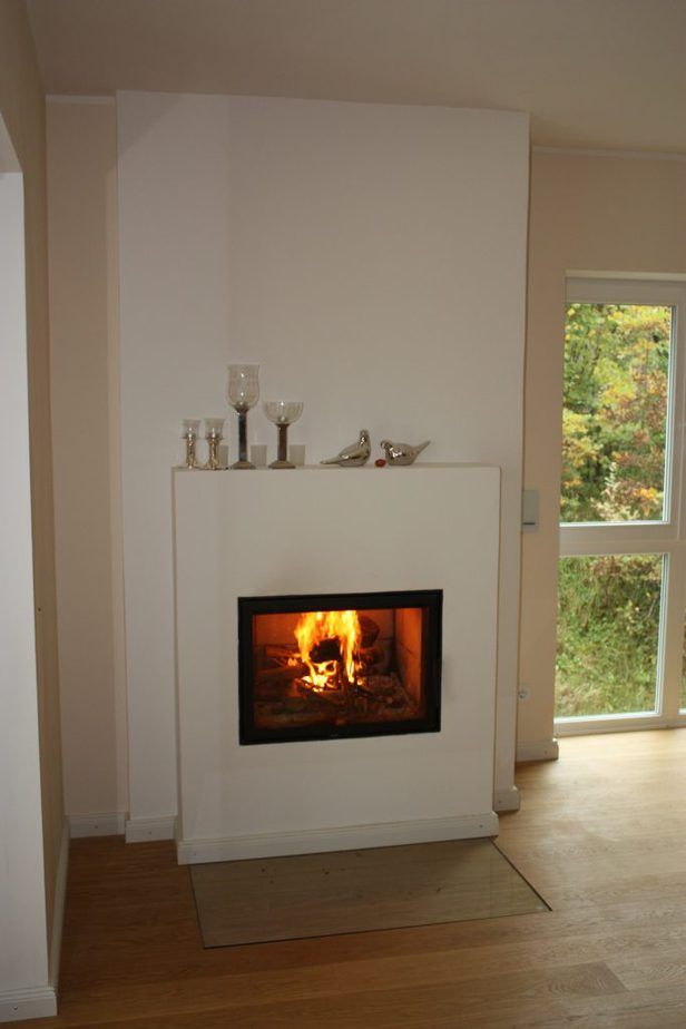 Modernes Wohnzimmer mit weißem Kamin und prasselndem Feuer neben einem hohen Fenster.