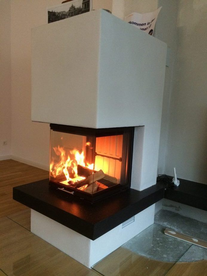 Moderner weißer Kamin mit offener Flamme und schwarzer Kaminplatte im Wohnzimmer.