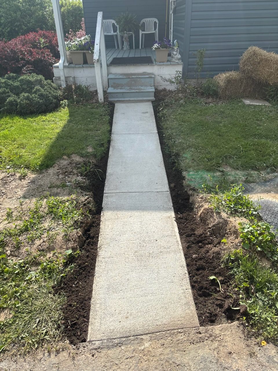 Concrete walkway leading to a front porch with steps, bordered by grass and shrubs.