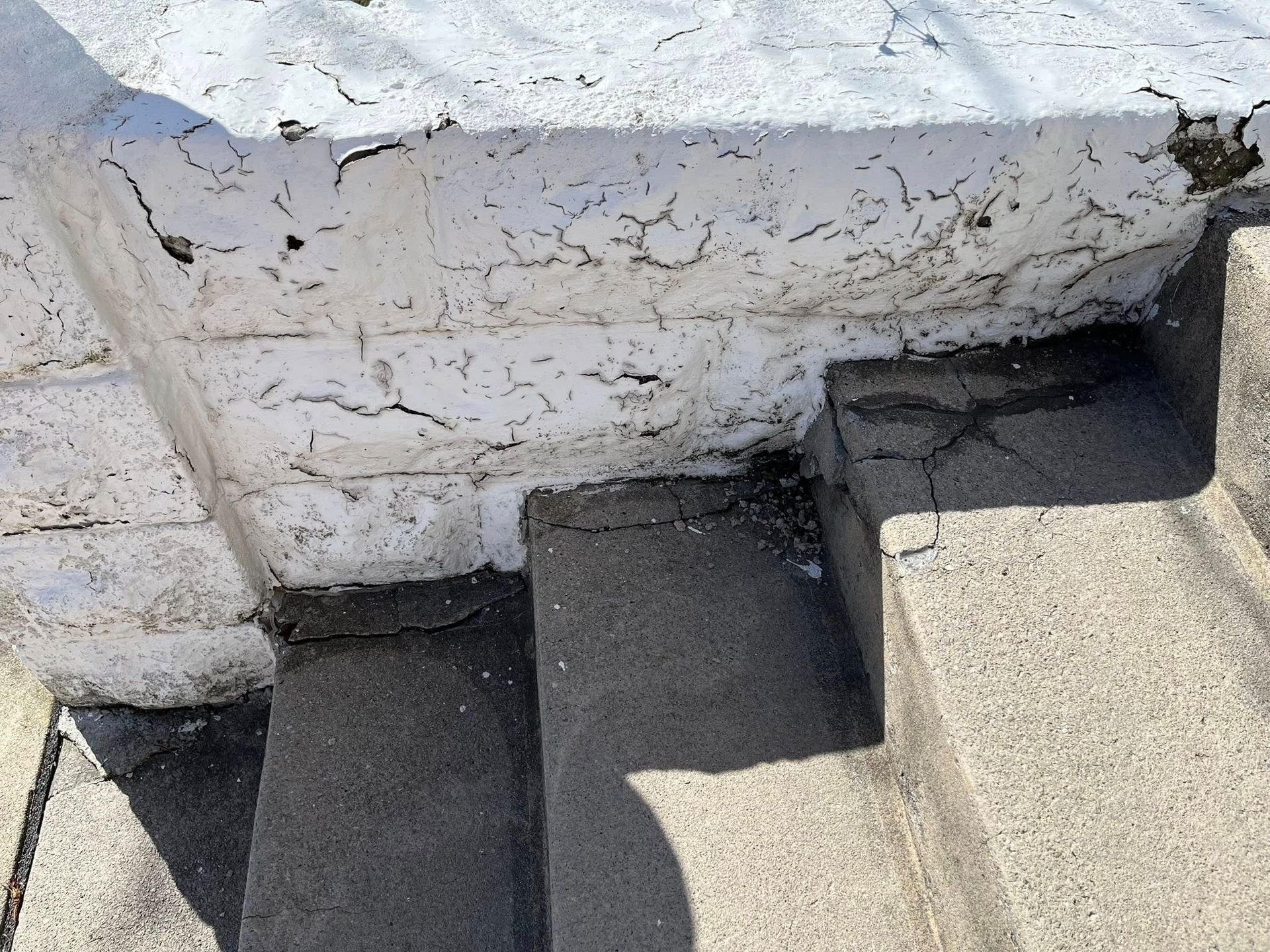 Concrete steps beside a weathered white wall in bright sunlight