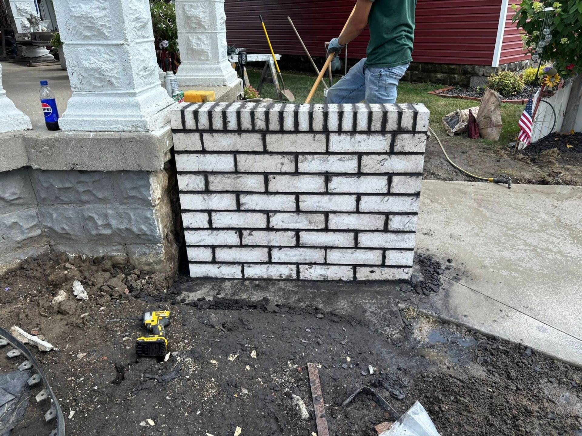 Partially built white brick wall beside a concrete walkway with a worker and tools nearby