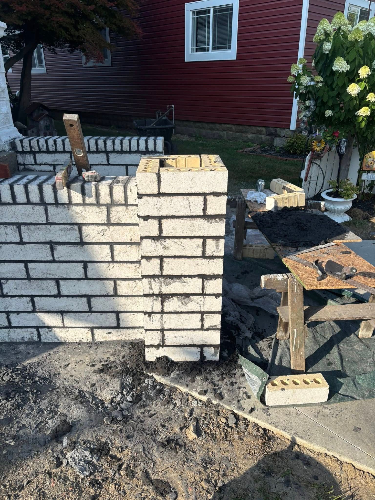Partially built white brick wall with a red house and garden flowers in the background