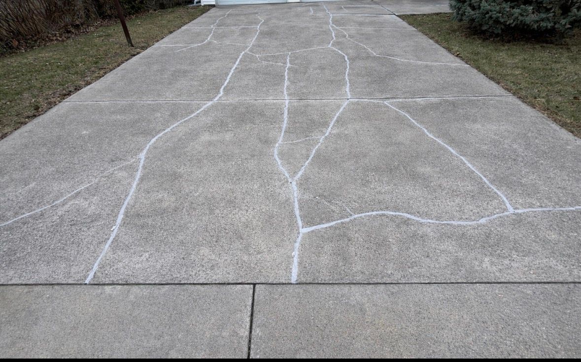 Cracked concrete driveway with white chalk lines marking sections.